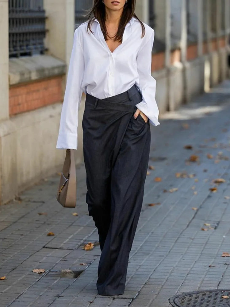 Woman in white collared shirt and casual suit pants holding brown handbag